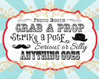 May include: A white sign with red and gold trim, announcing a photo booth. The sign reads "Photo Booth", "Grab a Prop", "Strike a Pose", "Serious or Silly", and "Anything Goes".