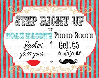May include: A white sign with red and blue stripes in the background. The sign says "Step Right Up to Noah Mason's Photo Booth". It also says "Ladies gloss your" with a red lipstick and "Gents comb your" with a black mustache.