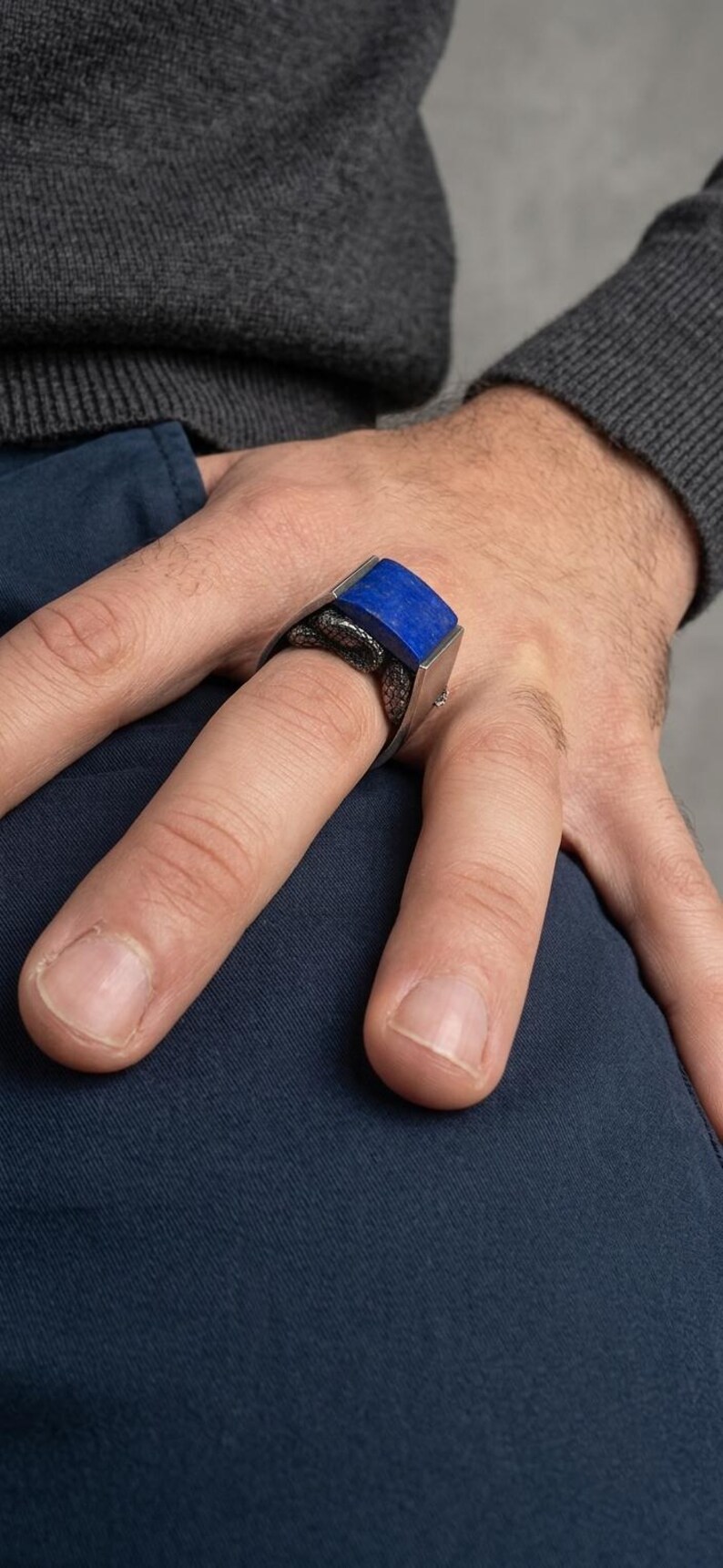 May include: A silver ring featuring a rectangular, deep blue lapis lazuli stone set horizontally. The band of the ring is designed with a textured, dark metallic snake motif that wraps around the finger, providing a detailed contrast to the smooth, vibrant blue stone.