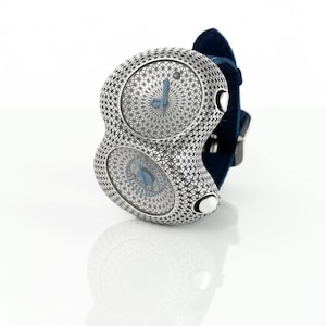 May include: A unique silver-toned wristwatch with two circular faces, each featuring a blue clock face and hands. The watch has a patterned design and is attached to a dark blue fabric band. The watch is displayed on a white surface.