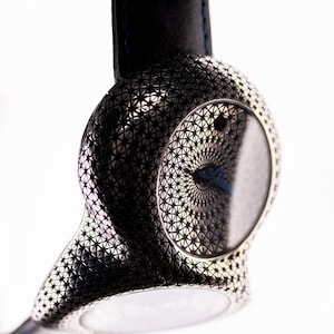 May include: A modern wristwatch with a black leather band and a silver-toned case. The case features a geometric pattern and a circular watch face with a blue hand. The watch is suspended against a white background.