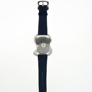 May include: A silver-toned wristwatch with a unique, abstract case design and a dark blue leather strap. The watch face features a circular pattern and is attached to a buckle closure. The strap has multiple adjustment holes.