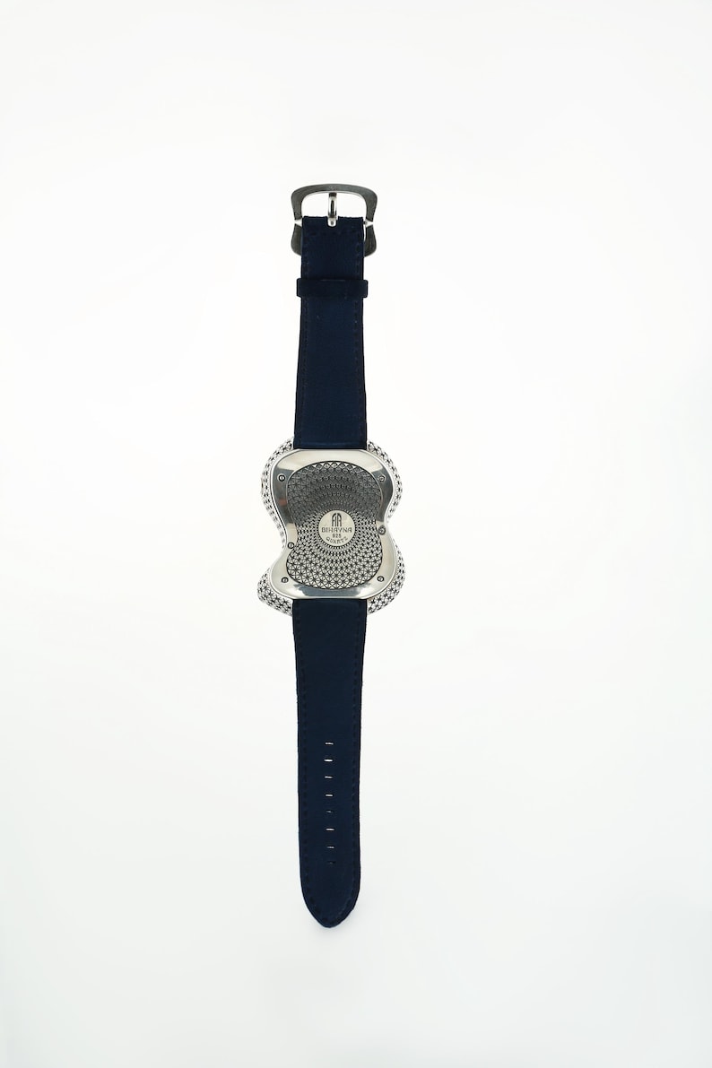 May include: A silver-toned wristwatch with a unique, abstract case design and a dark blue leather strap. The watch face features a circular pattern and is attached to a buckle closure. The strap has multiple adjustment holes.