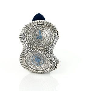 May include: A unique silver-toned wristwatch with two circular watch faces. The watch features a geometric pattern and blue hands. A dark blue band is attached to the top of the watch. The watch is displayed on a white surface.