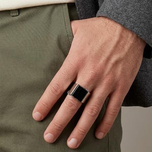 May include: A wide silver-toned metal ring featuring a smooth, rectangular black inlay centered on the band. The ring has a polished finish and a flat top surface, showcasing a clean, geometric design that sits prominently on the finger.