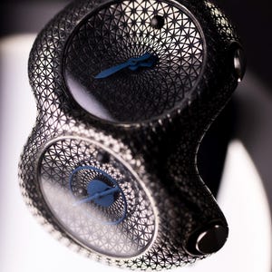 May include: A unique, dual-faced wristwatch with a geometric, open-worked design. The watch features a dark, metallic finish with blue hands and a detailed, patterned dial. The overall aesthetic is modern and intricate.
