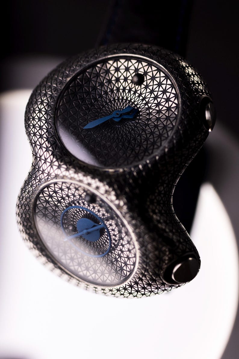May include: A unique, dual-faced wristwatch with a geometric, open-worked design. The watch features a dark, metallic finish with blue hands and a detailed, patterned dial. The overall aesthetic is modern and intricate.