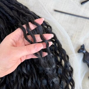 May include: Long, black synthetic hair extensions featuring a deep, wavy texture. The hair strands are dark, voluminous, and have a consistent crimped wave pattern throughout the length, showcasing a natural-looking matte finish and soft movement.