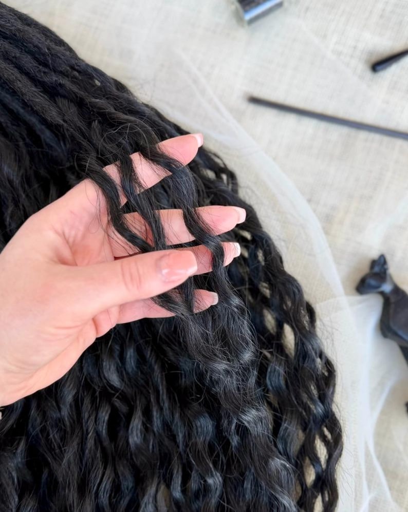 May include: Long, black synthetic hair extensions featuring a deep, wavy texture. The hair strands are dark, voluminous, and have a consistent crimped wave pattern throughout the length, showcasing a natural-looking matte finish and soft movement.