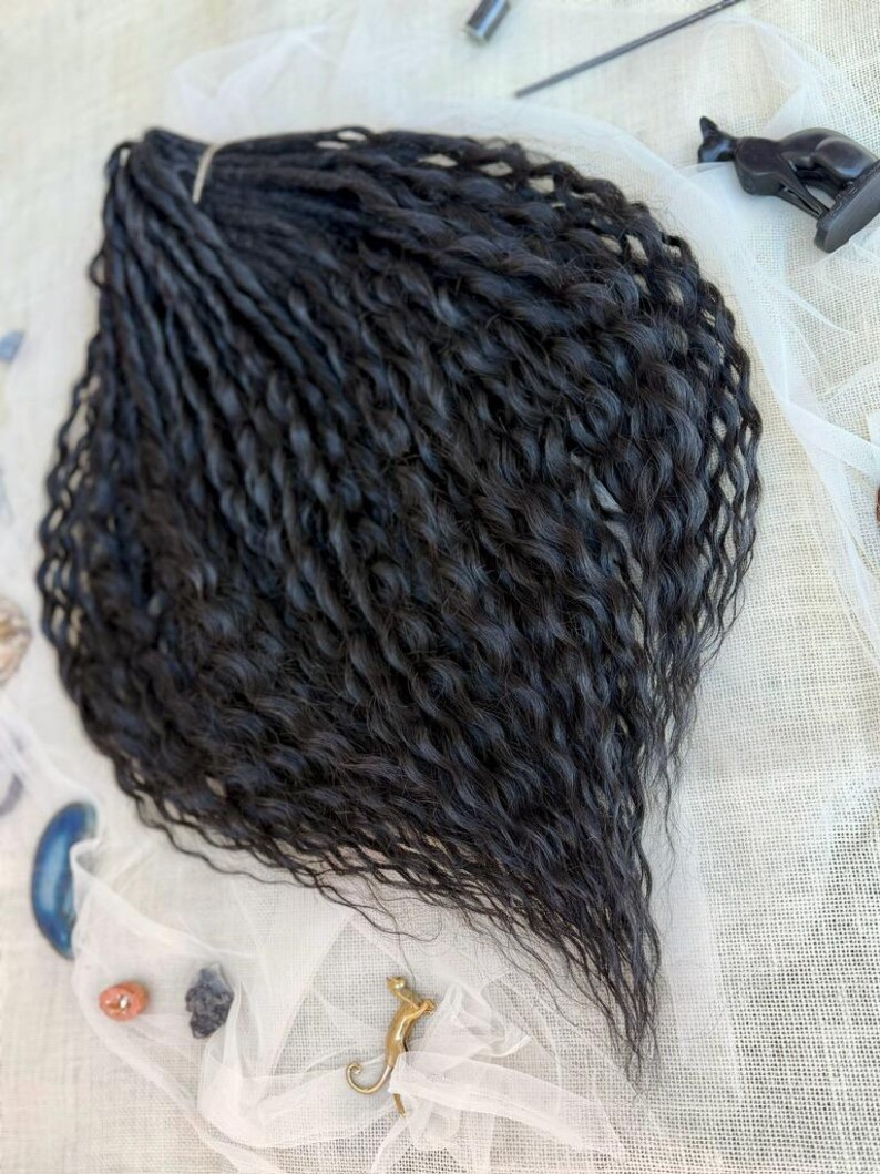 May include: A bundle of long, black, wavy hair extensions featuring a crimped texture. The strands are gathered at the top with a small band, creating a fan-like shape that tapers toward the bottom, showcasing a consistent dark color throughout.