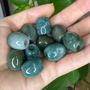 May include: A collection of ten smooth, barrel-shaped moss agate beads featuring deep forest green hues with translucent, cloudy white inclusions. Each bead has a central hole, polished surfaces, and a rounded, cylindrical form with varied patterns.
