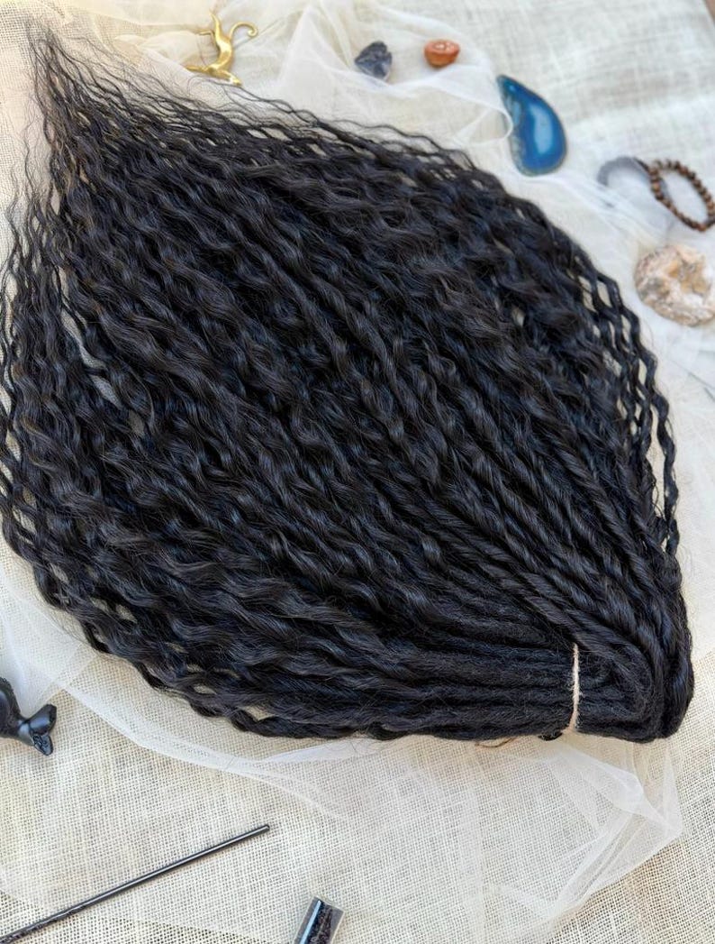 May include: A bundle of black synthetic hair extensions featuring a wavy, textured pattern. The individual strands are gathered and secured at one end with a light-colored band, creating a uniform, voluminous appearance with a consistent dark color.
