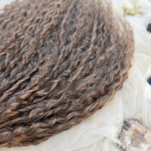 May include: A collection of long, wavy hair extensions featuring a blend of light brown and dark brown tones. The strands are tightly curled with a consistent texture throughout, showcasing a multi-dimensional color palette with highlights and lowlights.