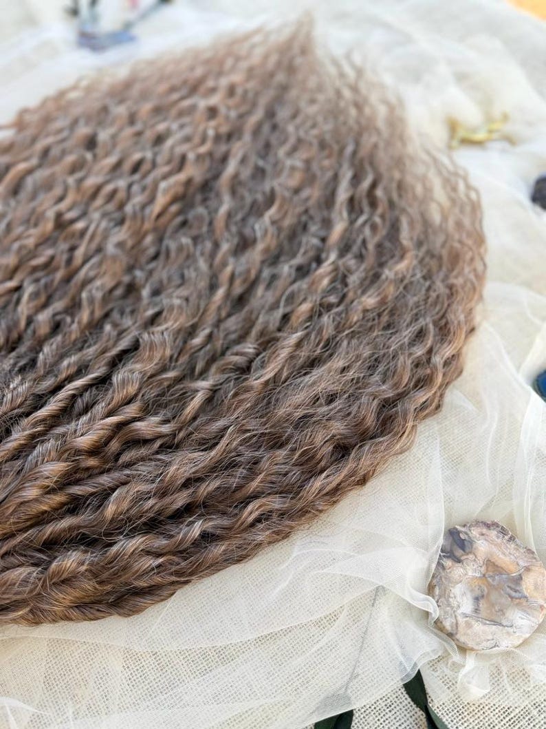 May include: A collection of long, wavy hair extensions featuring a blend of light brown and dark brown tones. The strands are tightly curled with a consistent texture throughout, showcasing a multi-dimensional color palette with highlights and lowlights.