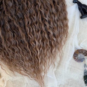 May include: A cascade of long, wavy brown hair extensions featuring multi-tonal highlights. The hair has a crimped, textured appearance with a deep brown base and lighter brown streaks throughout, creating a voluminous and layered look.
