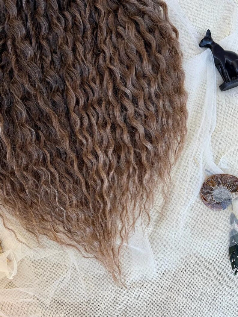 May include: A cascade of long, wavy brown hair extensions featuring multi-tonal highlights. The hair has a crimped, textured appearance with a deep brown base and lighter brown streaks throughout, creating a voluminous and layered look.
