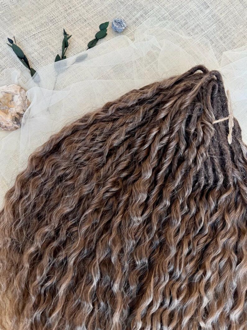 May include: A bundle of brown hair extensions featuring a wavy, twisted texture. The strands exhibit a multi-tonal brown color palette with lighter highlights throughout, secured at the top with a thin, dark brown cord tied in a small knot.