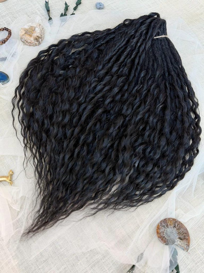 May include: A bundle of black hair extensions featuring a wavy, textured pattern. The strands are gathered at the top with a light-colored string, creating a fan-like shape that cascades downward with defined, crimped curls throughout the length.