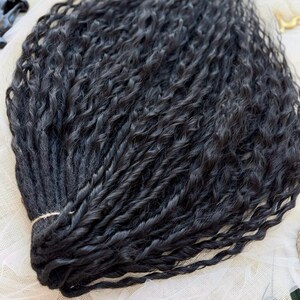May include: A bundle of black hair extensions featuring a tight, wavy, and twisted texture. The individual strands are gathered together at one end and secured with a thin, light-colored string, creating a uniform and voluminous appearance.