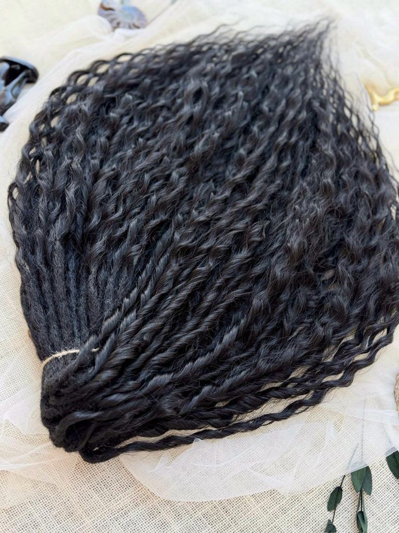 May include: A bundle of black hair extensions featuring a tight, wavy, and twisted texture. The individual strands are gathered together at one end and secured with a thin, light-colored string, creating a uniform and voluminous appearance.