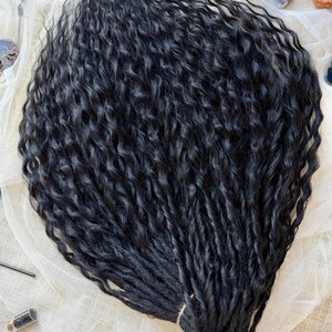 May include: A bundle of long, black hair extensions featuring a deep, wavy texture. The strands are dark, uniform in color, and arranged in a dense, flowing cluster that highlights the consistent curl pattern throughout the entire length.