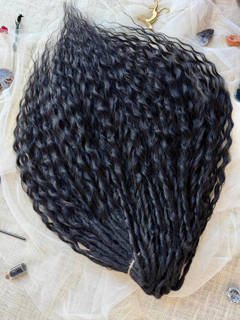 May include: A bundle of long, black hair extensions featuring a deep, wavy texture. The strands are dark, uniform in color, and arranged in a dense, flowing cluster that highlights the consistent curl pattern throughout the entire length.