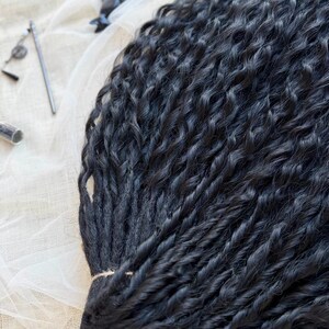 May include: A bundle of long, black synthetic hair extensions featuring a tight, wavy, and twisted texture. The strands are gathered together at one end with a thin string, showcasing a uniform dark color and a consistent, crimped, wavy pattern throughout.