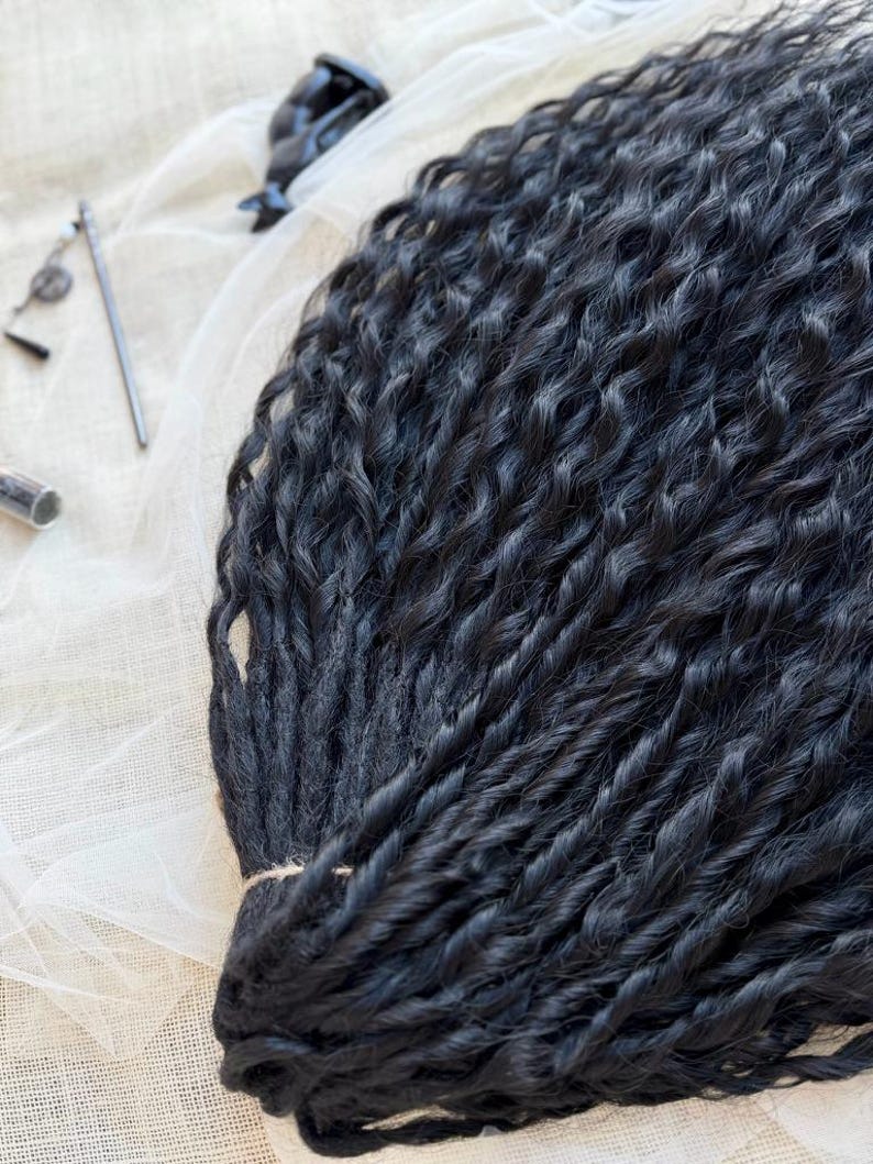 May include: A bundle of long, black synthetic hair extensions featuring a tight, wavy, and twisted texture. The strands are gathered together at one end with a thin string, showcasing a uniform dark color and a consistent, crimped, wavy pattern throughout.