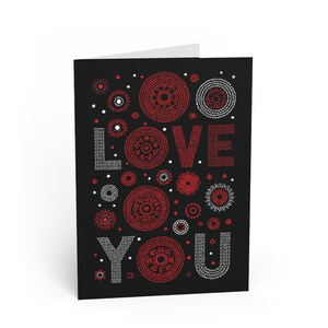 Peut inclure: Carte de vœux pliée avec un fond noir. Les mots "LOVE YOU" sont épelés en points blancs et rouges. La carte présente des motifs circulaires rouges et blancs de tailles variées.