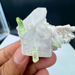 Peut inclure: Un amas de cristaux de quartz transparents avec plusieurs petits cristaux vert clair. Le quartz a une structure cristalline et se détache sur un fond blanc. Les cristaux sont tenus dans une main.