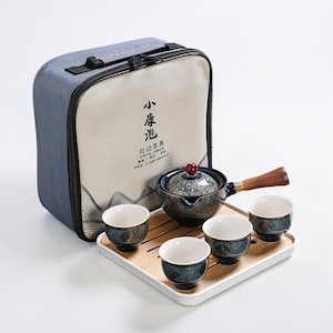 May include: A ceramic tea set in blue and white, featuring a teapot with a wooden handle and four cups, displayed on a bamboo tray. The set includes a carrying case with Chinese characters.