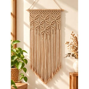 May include: A beige macrame wall hanging featuring a series of interconnected circular knot patterns suspended from a horizontal wooden dowel, with long, straight fringe extending downward to form a pointed bottom edge.
