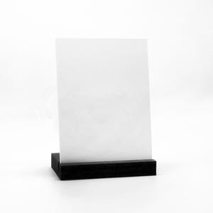 Könnte beinhalten: Ein weißes rechteckiges Schild wird von einem schwarzen rechteckigen Sockel gehalten. Das Schild ist leer und steht aufrecht. Der Sockel ist einfarbig, mattschwarz. Der Hintergrund ist einfarbig weiß.