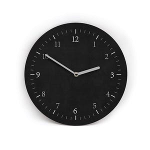 Könnte beinhalten: Eine runde, schwarze Wanduhr mit weißen Ziffern und Zeigern. Das Zifferblatt hat eine strukturierte Oberfläche. Die silbernen Zeiger zeigen die Uhrzeit etwa 10:10 Uhr an. Die Uhr hat ein schlichtes, modernes Design.