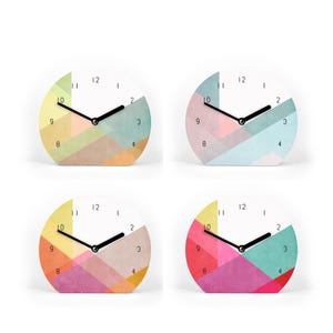 Könnte beinhalten: Vier kleine, runde Uhren mit weißen Zifferblättern und schwarzen Zeigern. Jede Uhr hat ein farbenfrohes geometrisches Design in Rosa-, Blau-, Gelb- und Orangetönen. Die Uhren sind vor einem weißen Hintergrund.