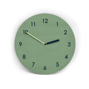 Könnte beinhalten: Eine runde Wanduhr mit einem salbeigrünen Zifferblatt und dunkelblauen Ziffern von eins bis zwölf. Die Uhr hat einen kurzen, dicken dunkelblauen Stundenzeiger und einen langen, schlanken hellen lindgrünen Minutenzeiger in der Mitte.