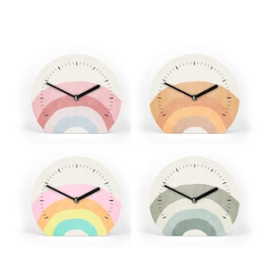 Könnte beinhalten: Vier kleine, runde Uhren mit weißem Hintergrund und Regenbogen-Design. Jede Uhr hat ein anderes pastellfarbenes Regenbogenschema, mit schwarzen Zeigern und einem minimalistischen Design. Die Uhren sind ein dekorativer Einrichtungsgegenstand.