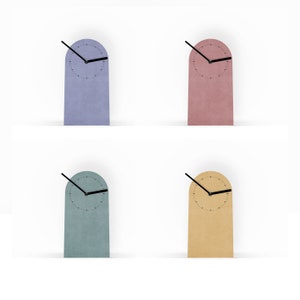 Könnte beinhalten: Vier minimalistische Schreibtischuhren in Pastellfarben: Lavendel, Rosa, Türkis und Beige. Jede Uhr hat einen rechteckigen Sockel mit abgerundeter Oberseite, ein schwarzes Zifferblatt und schwarze Zeiger. Die Uhren stehen auf einer weißen Oberfläche.