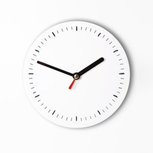 Könnte beinhalten: Eine minimalistische weiße Wanduhr mit schwarzen Zeigern und Stundenmarkierungen. Der Sekundenzeiger ist rot. Das Zifferblatt hat ein schlichtes, klares Design, ideal für moderne Dekoration.