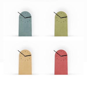 Könnte beinhalten: Vier minimalistische Uhren in Blau, Grün, Beige und Rot. Jede Uhr hat einen rechteckigen Sockel mit gewölbtem Oberteil, schwarzen Zeigern und schwarzen Ziffern. Die Uhren sind etwa 15 cm hoch.