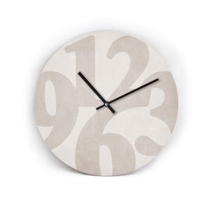 Könnte beinhalten: Eine runde Wanduhr mit cremefarbenem Zifferblatt und großen, beigen Ziffern. Die Zahlen 12, 3, 6 und 9 sind deutlich sichtbar. Schwarze Zeiger zeigen die Uhrzeit an. Die Uhr ist ein dekoratives Element für die Inneneinrichtung, ca. 30 cm im Durchmesser.