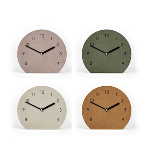Könnte beinhalten: Vier kleine, runde Uhren in neutralen Farben: Taupe, Olivgrün, Creme und Braun. Jede Uhr hat schwarze Zeiger und schwarze Ziffern. Die Uhren werden vor einem weißen Hintergrund angezeigt.