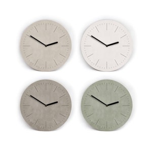 Könnte beinhalten: Vier runde Wanduhren in neutralen Farben: Hellgrau, Weiß, Grau und Grün. Jede Uhr hat ein minimalistisches Design mit schwarzen Zeigern und Markierungen. Die Uhren werden vor einem weißen Hintergrund präsentiert.