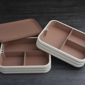 May include: Three-piece storage set with a rectangular lid and two divided trays. The trays have a white exterior and a light brown interior. The lid is light brown. The set is designed for organizing small items.