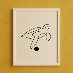 Puede incluir: Una impresión artística minimalista enmarcada con un dibujo de línea negra continua sobre un fondo blanquecino. La obra de arte incluye un círculo negro y formas abstractas, enmarcada en blanco contra una pared amarilla.