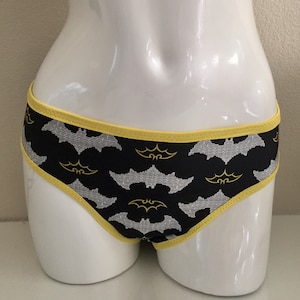 Może przedstawiać: Czarne majtki z ż&oacute;łtym wykończeniem i powtarzającym się wzorem białych i ż&oacute;łtych nietoperzy.