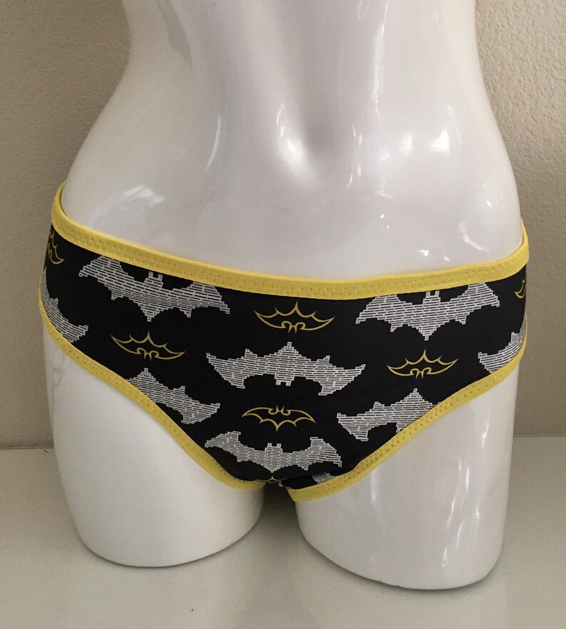 Może przedstawiać: Czarne majtki z ż&oacute;łtym wykończeniem i powtarzającym się wzorem białych i ż&oacute;łtych nietoperzy.