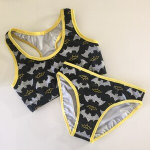 Może przedstawiać: Czarny komplet bielizny z ż&oacute;łtą lam&oacute;wką i nadrukiem nietoperzy. G&oacute;rna część to top sportowy.