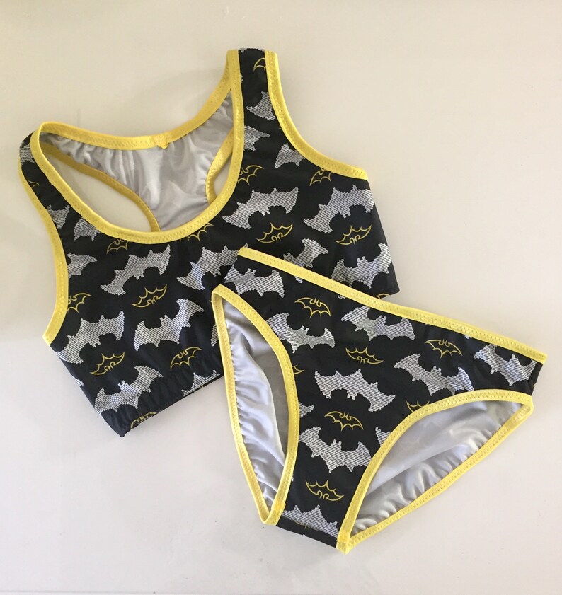 Może przedstawiać: Czarny komplet bielizny z ż&oacute;łtą lam&oacute;wką i nadrukiem nietoperzy. G&oacute;rna część to top sportowy.
