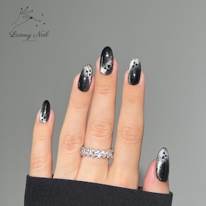 May include: Oval-shaped black and silver nail art with a sparkling design. The nails feature a glossy black base with silver glitter accents. A silver ring is on the ring finger. The image includes the text "Luxury Nail Art Crafts".